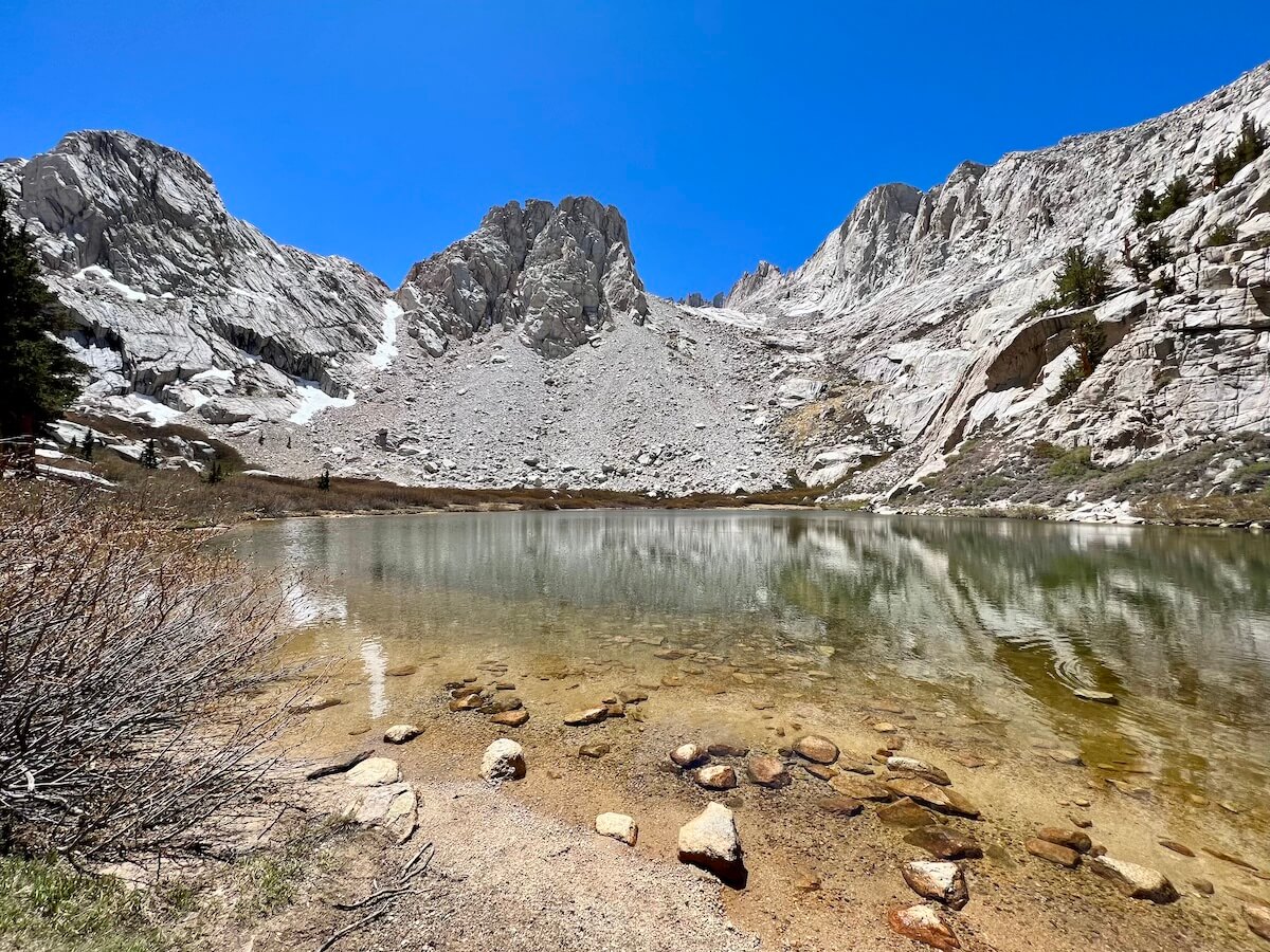 A peaceful view of Mirror Lake on the Mount Whitney Trail, with clear reflections of the surrounding rocky terrain and sky.