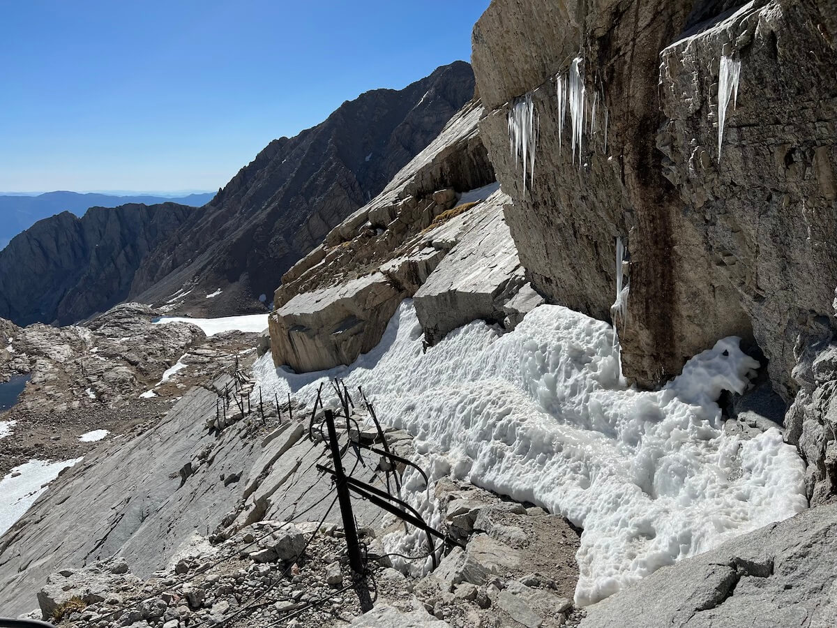 Snow-covered cable section on the 99 switchbacks of the Mount Whitney Trail during the shoulder season, with icicles and snow accumulation along the trail.