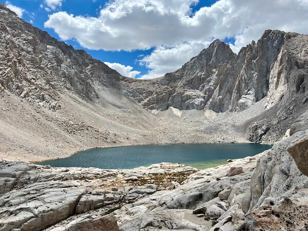 Consultation Lake at 12,000 feet on the Mount Whitney Main Trail, surrounded by rugged granite peaks under a partly cloudy sky.