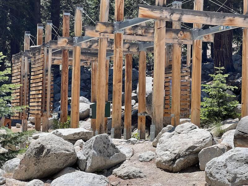 Iconic wooden and metal arches at the Whitney Portal, surrounded by rocks and trees, marking the beginning of the Mount Whitney trail.