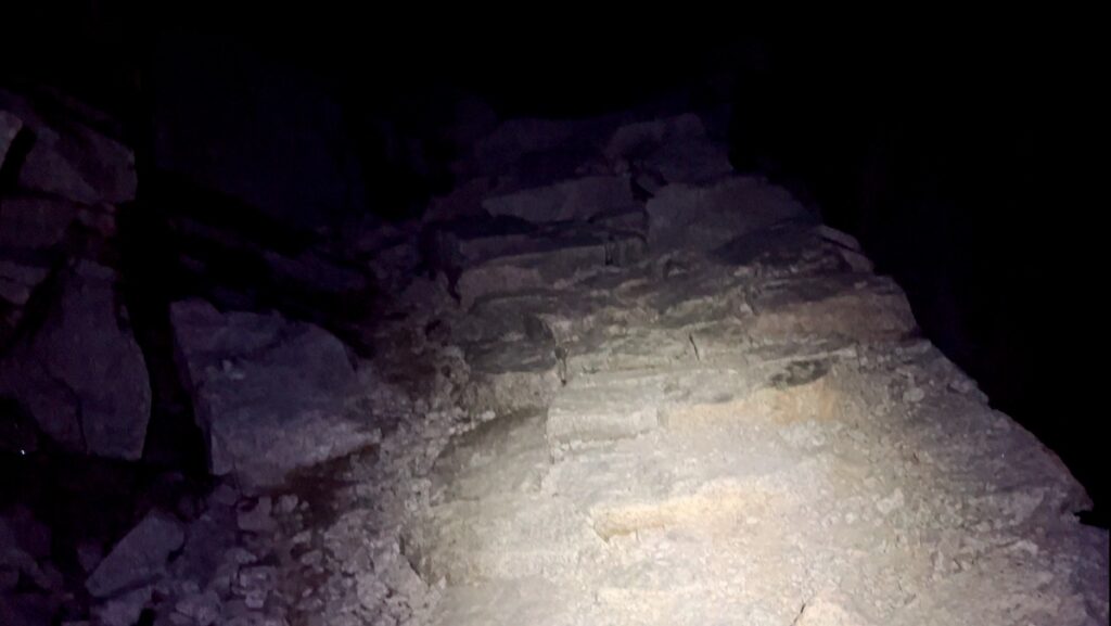 Dark rocky path up the 99 switchbacks on Mount Whitney main trail, illuminated by a headlamp in pitch-black darkness.