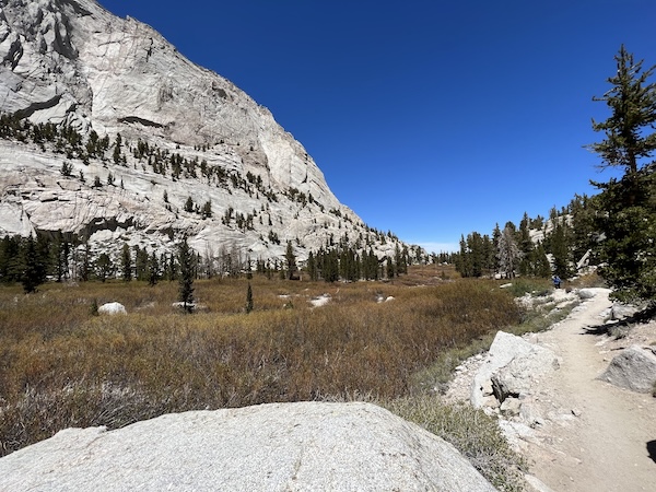 Bighorn Park on the Mount Whitney Main Trail, featuring open meadows, granite cliffs, and a winding dirt trail under a clear blue sky. Photo from shoulder season trip.
