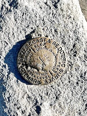 Bronze geodetic marker embedded in granite at the summit of Mount Whitney, inscribed with U.S. Coast & Geodetic Survey information and displaying the older elevation of 14,494 feet.
